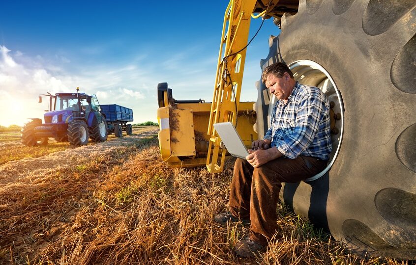 rolnik z laptopem na polu przy traktorze